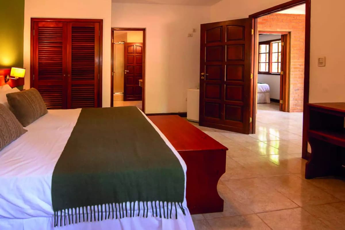 A hotel room with a bed, a bench, and two doors leading to other rooms.