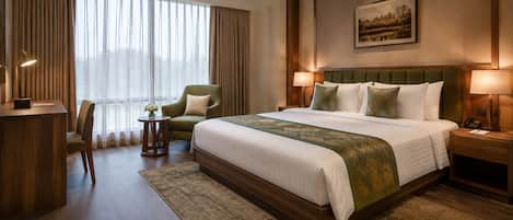 A hotel room with a large bed, a desk, a chair, and a view of the outdoors through the window.