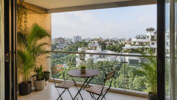 A balcony with a table and chairs, potted plants, and a view of a cityscape.