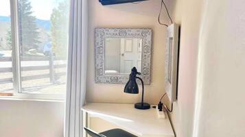 A hotel room with a bed, a desk with a chair, a television mounted on the wall, and a window with curtains.