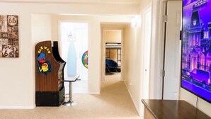 A living room with a flat-screen TV on a wooden cabinet, a dartboard, and a wall with a colorful poster. - Private Suite - Pacman Arcade, USAFA, Yard, AC, Espresso Machine, Kids Playroom (Monument)