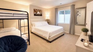 A bedroom with a bunk bed, a single bed, a bedside table with a lamp, a chair, and a window with curtains. - Private Suite - Pacman Arcade, USAFA, Yard, AC, Espresso Machine, Kids Playroom (Monument)