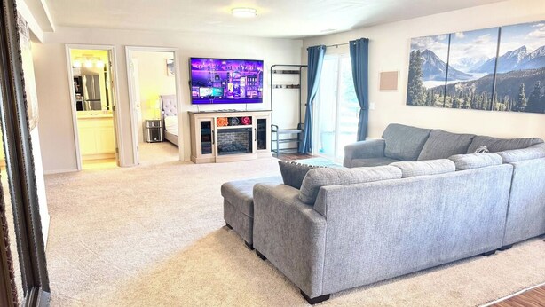 A living room with a grey sofa, a flat-screen TV, a fireplace, and a mountain landscape painting. - Private Suite - Pacman Arcade, USAFA, Yard, AC, Espresso Machine, Kids Playroom (Monument)