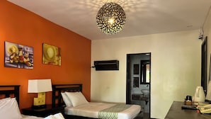 Habitación de hotel con dos camas, un escritorio, una lámpara, un televisor montado en la pared y una obra de arte en la pared.