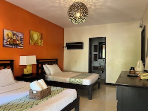A hotel room with two beds, a desk, a lamp, a wall-mounted TV, and artwork on the wall. - Puerto Del Sol Beach Resort And Hotel Club (Bolinao)
