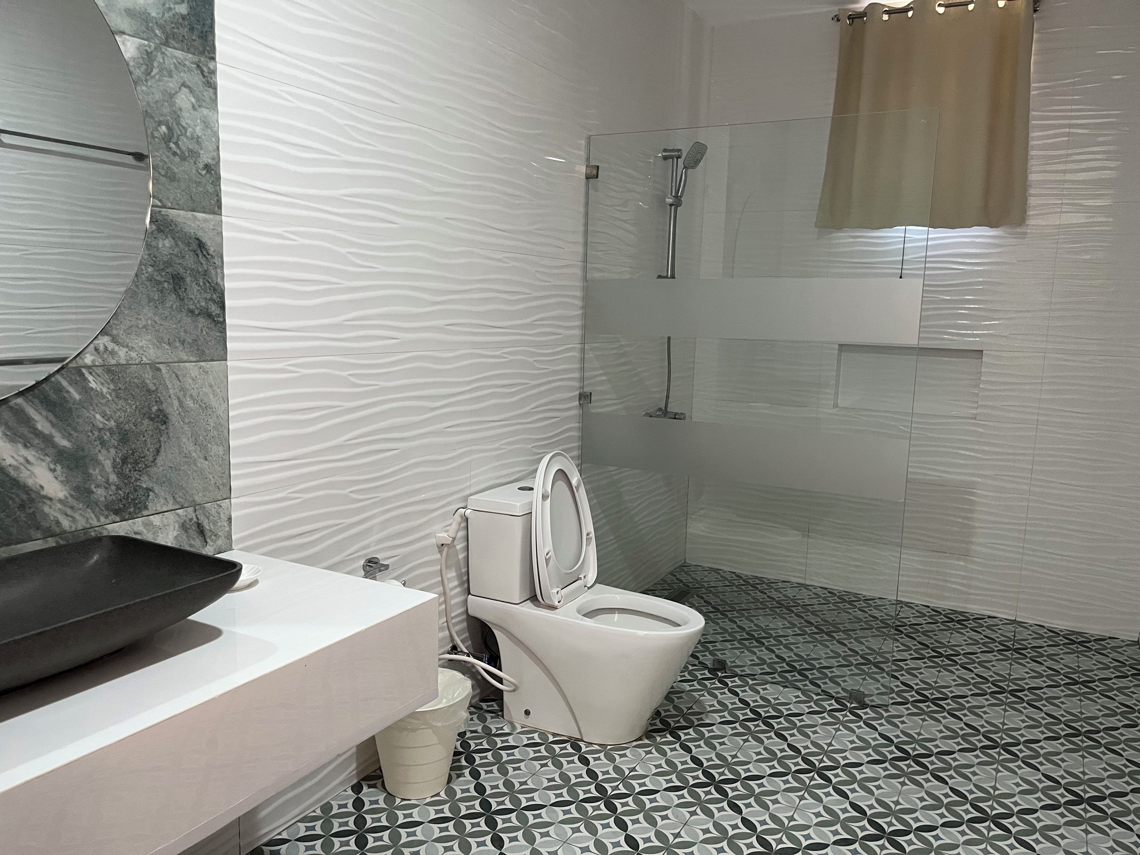 Un baño con diseño moderno, que cuenta con pared de mármol, lavamanos, inodoro y zona de ducha.