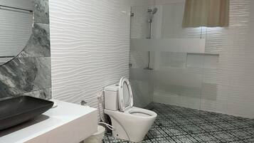 Un baño con diseño moderno, que cuenta con pared de mármol, lavamanos, inodoro y zona de ducha.