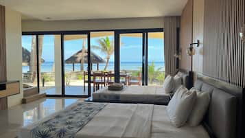 A hotel room with a large bed, a view of the beach, and a dining area with a table and chairs.