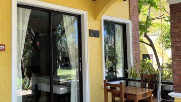 A covered patio area with a sliding glass door leading to a balcony, a wooden table and chairs, and potted plants.