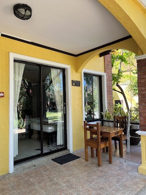 A covered patio area with a sliding glass door leading to a balcony, a wooden table and chairs, and potted plants.