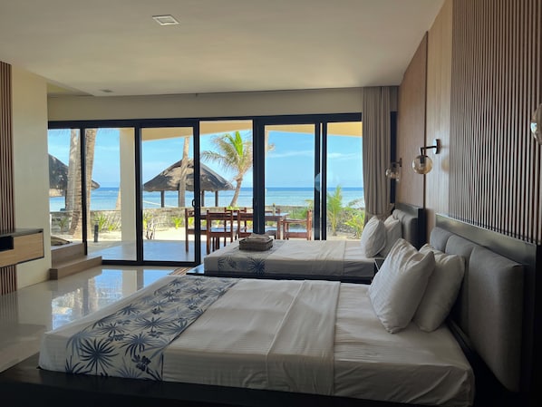 A hotel room with a large bed, a view of the beach, and a dining area with a table and chairs. - Puerto Del Sol Beach Resort And Hotel Club (Bolinao)