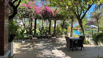An outdoor patio area with a table and chairs, surrounded by potted plants and trees with pink flowers.