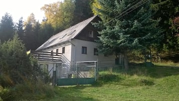 A two-story house with a sloped roof, surrounded by trees and a fenced yard.