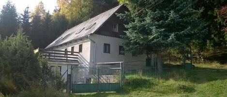 A two-story house with a sloped roof, surrounded by trees and a fenced yard.