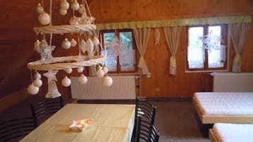 A wooden interior with a dining table, chairs, a hanging ornament, and two beds.