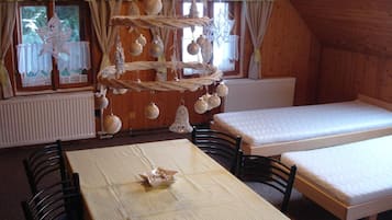 A room with a wooden interior, a table with a checkered tablecloth, two beds, and a hanging ornament decoration.