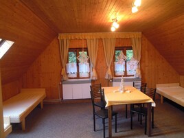 Un acogedor cuarto ático con techo inclinado de madera, una mesa con sillas, un banco y una ventana con cortinas.