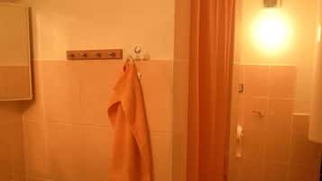 A bathroom with a toilet, a towel rack with a towel, a shower curtain, and a light fixture.