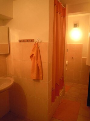 Un baño con inodoro, toallero con toalla, cortina de ducha y lámpara.