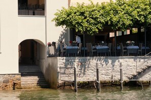 Un restaurante frente al agua con terraza, una escalera de piedra y vistas al mar.