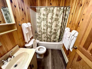 Un baño con paneles de madera, inodoro, lavamanos y cortina de ducha.