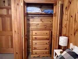Um guarda-roupa de madeira com várias gavetas e uma cama com manta xadrez.