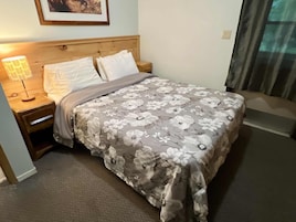 Quarto de hotel com cama, mesa de cabeceira com luminária e janela com cortinas.