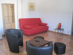 Un salón con un sofá rojo, dos sillas negras, una mesa de centro de madera y una mesita auxiliar con un jarrón.