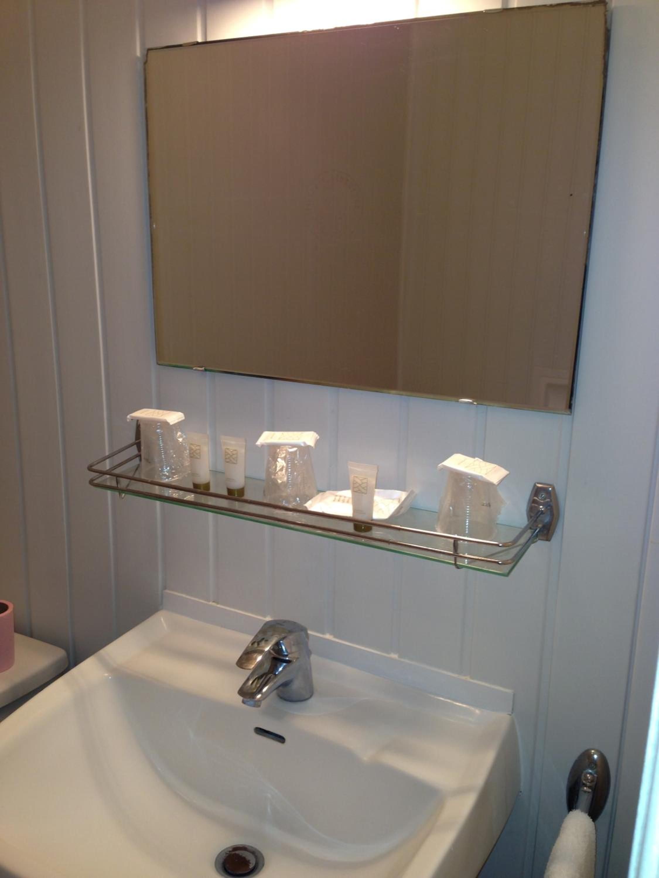 Une salle de bain avec un lavabo blanc, un miroir au-dessus et une étagère contenant des articles de toilette.