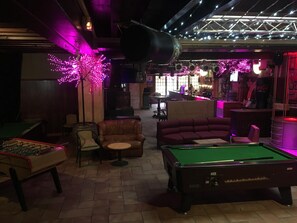 Una mesa de billar, una mesa de futbolín y una mesa de billar americano en una sala con iluminación morada.