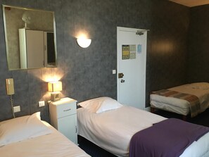 Habitación de hotel con dos camas, una lámpara de noche, un espejo, una puerta con un tablón de anuncios y un teléfono.
