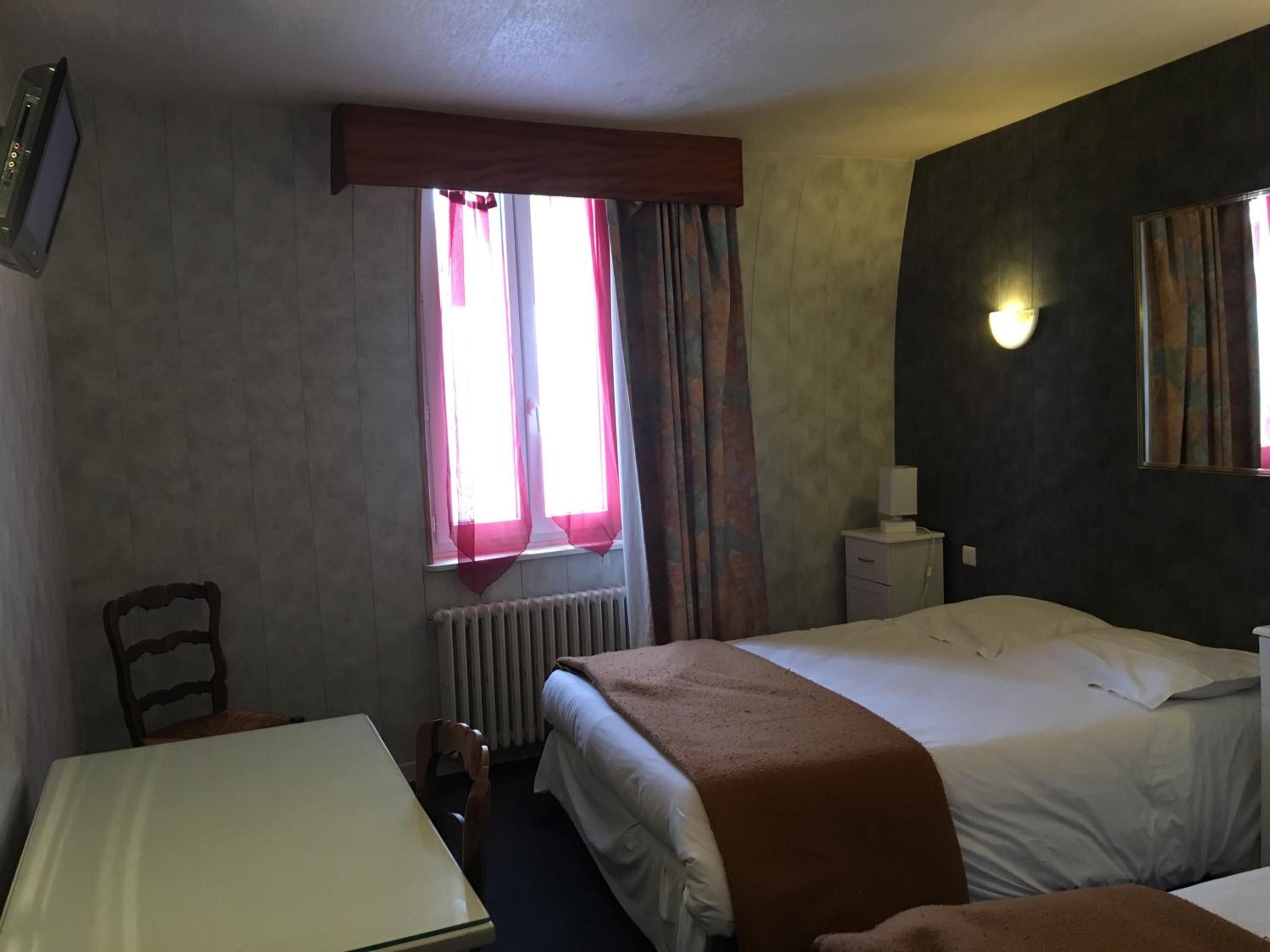 Une chambre d’hôtel avec deux lits, une table, une chaise, un radiateur et une fenêtre avec des rideaux.