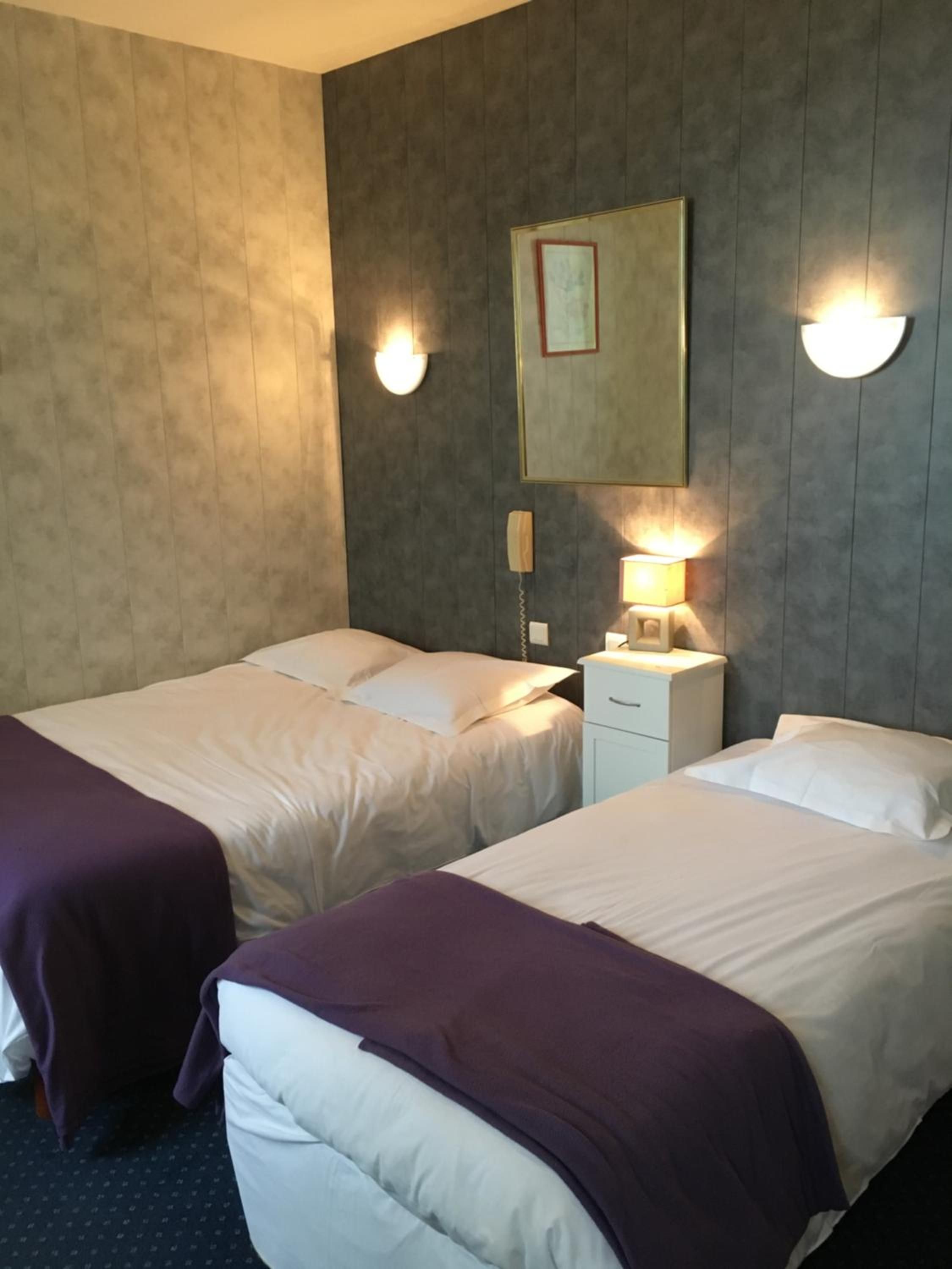 Ein Hotelzimmer mit zwei Betten, einem Nachttisch mit Lampe und einem an der Wand befestigten Telefon.