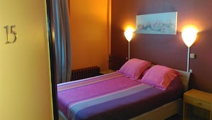 Quarto de hotel com cama, duas luminárias de cabeceira, radiador e um quadro na parede.