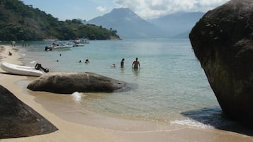 Uma praia com água cristalina, pessoas nadando e barcos.