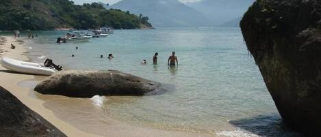 Una playa con agua cristalina, gente nadando y barcos.