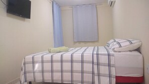Uma cama de solteiro com colcha listrada, um travesseiro e uma toalha enrolada no chão.