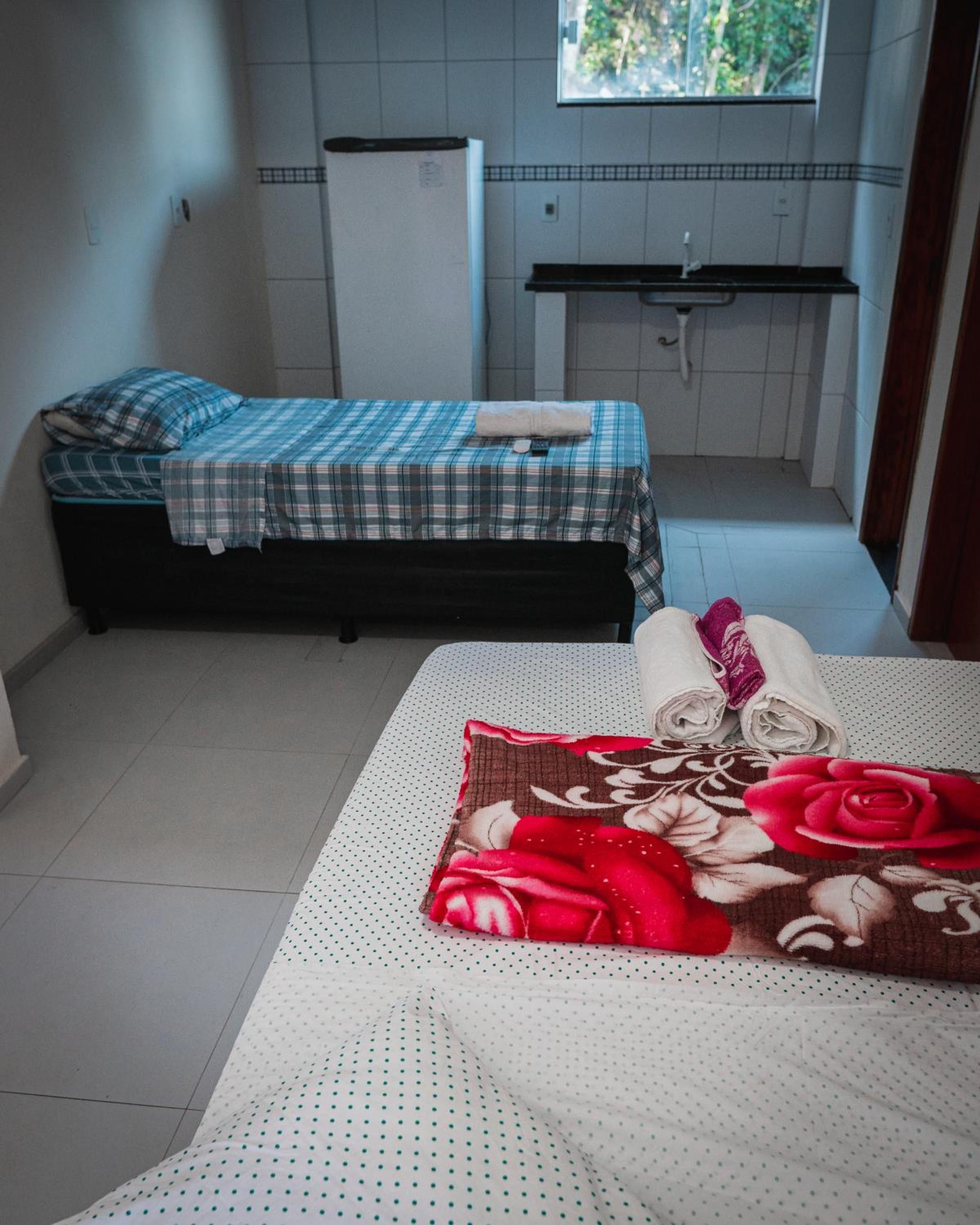 Um quarto pequeno com cama, um banco, uma cozinha compacta e uma janela.