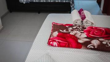 Um quarto pequeno com cama, um banco, uma cozinha compacta e uma janela.