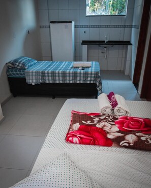 Um quarto pequeno com cama, um banco, uma cozinha compacta e uma janela.