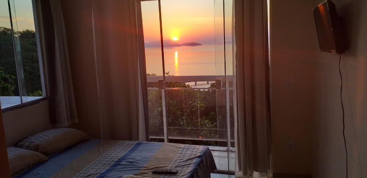 Quarto com cama, cortinas e vista do pôr do sol sobre a água.