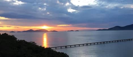A sunset over a calm body of water with a bridge in the foreground.
