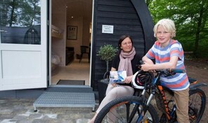 A person sitting on a bicycle outside a building with a door open to the inside. - Sportspark Blaavandshuk Resort (Oksbol)