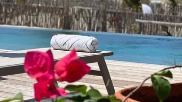 Um deck de madeira com piscina, toalha branca e flores cor-de-rosa.