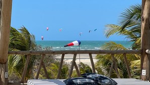 Una terrassa de fusta amb un llit, vista a la platja i una bandera.