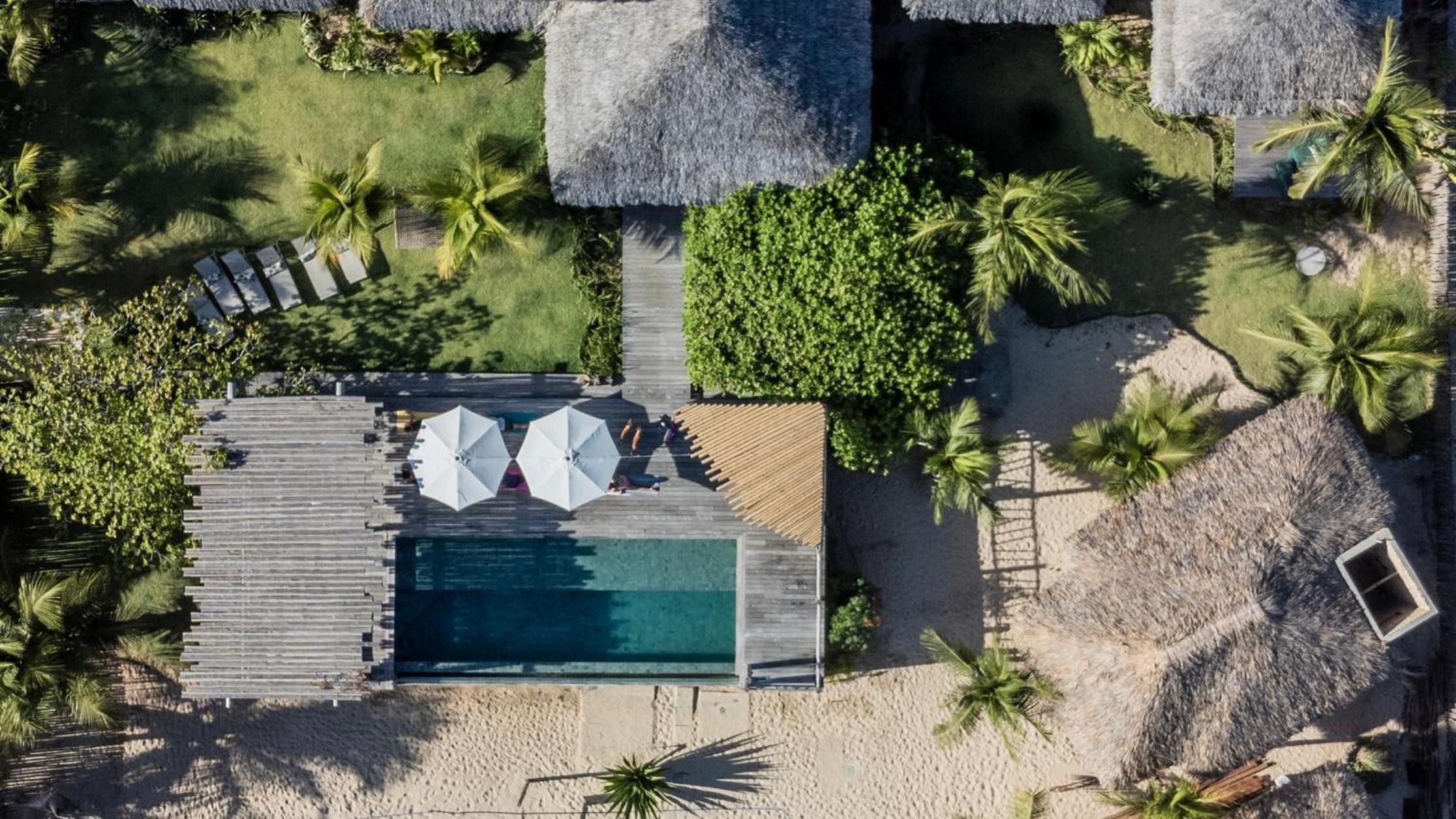 Vista aérea de um resort com piscina, área de descanso e construções com telhados de palha.
