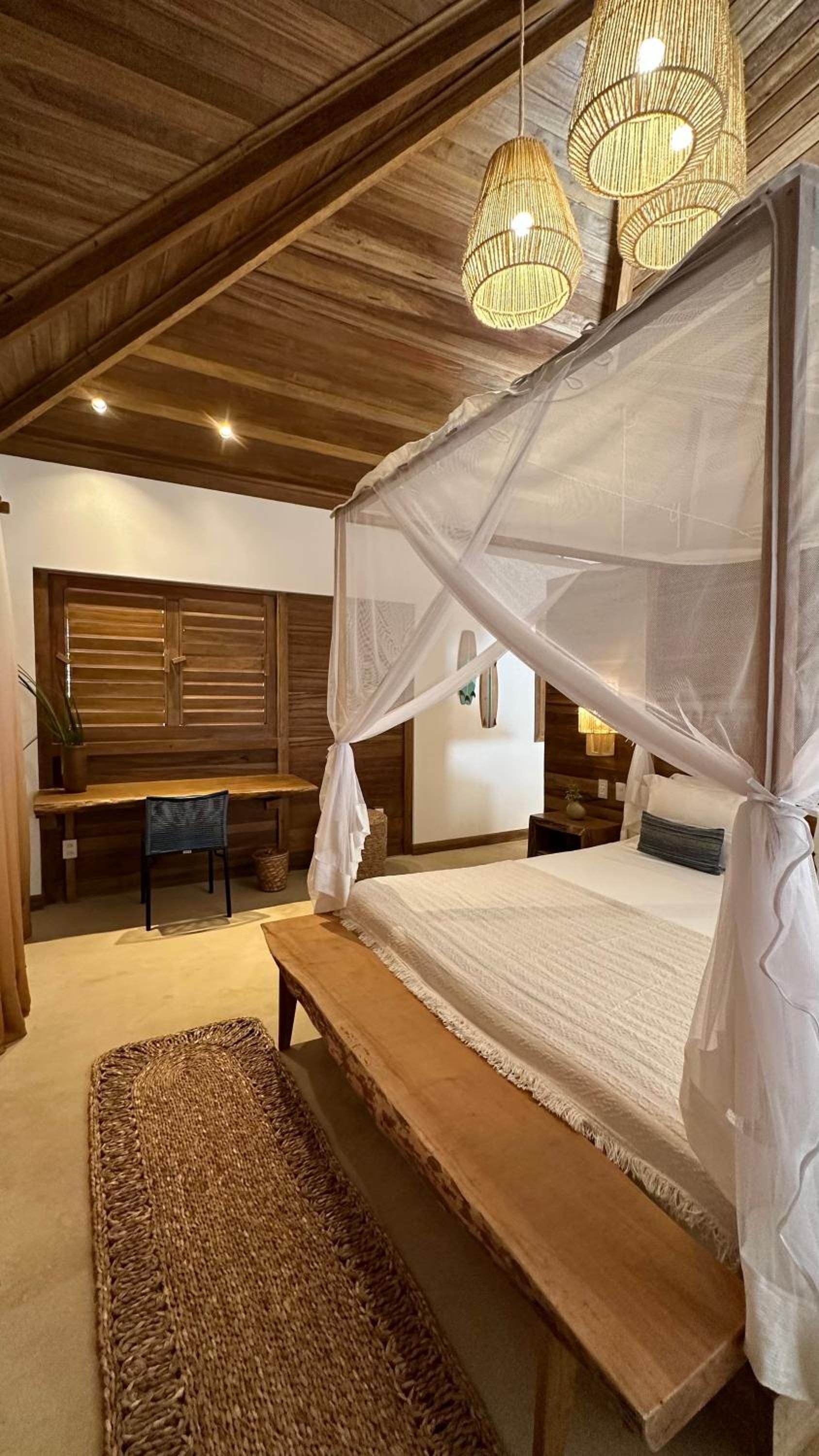 Quarto com cama de dossel, vigas de madeira no teto e tapete tecido.