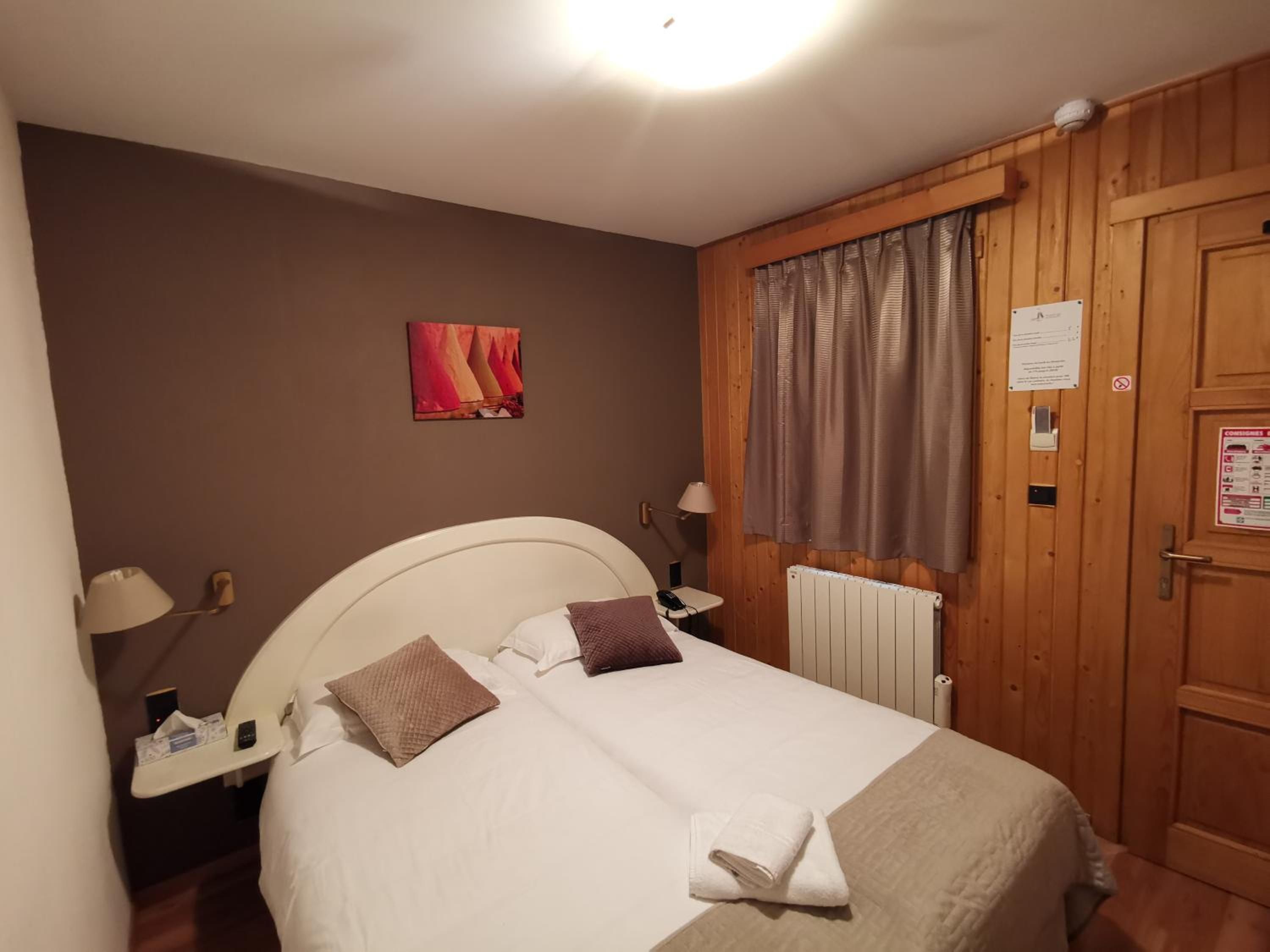 Ein Hotelzimmer mit einem Bett, Nachttischlampen, einem Heizkörper, einer Tür mit einem Hinweis und einem Wandbild.