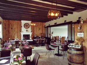 Interior de restaurante con paredes de madera, varias mesas de comedor y lámparas colgantes.