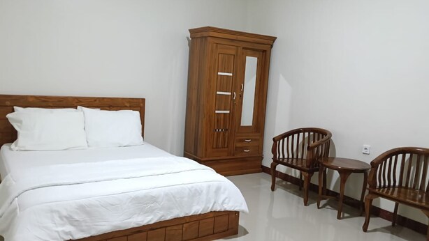 A bedroom with a bed, wooden wardrobe, and two wooden chairs.